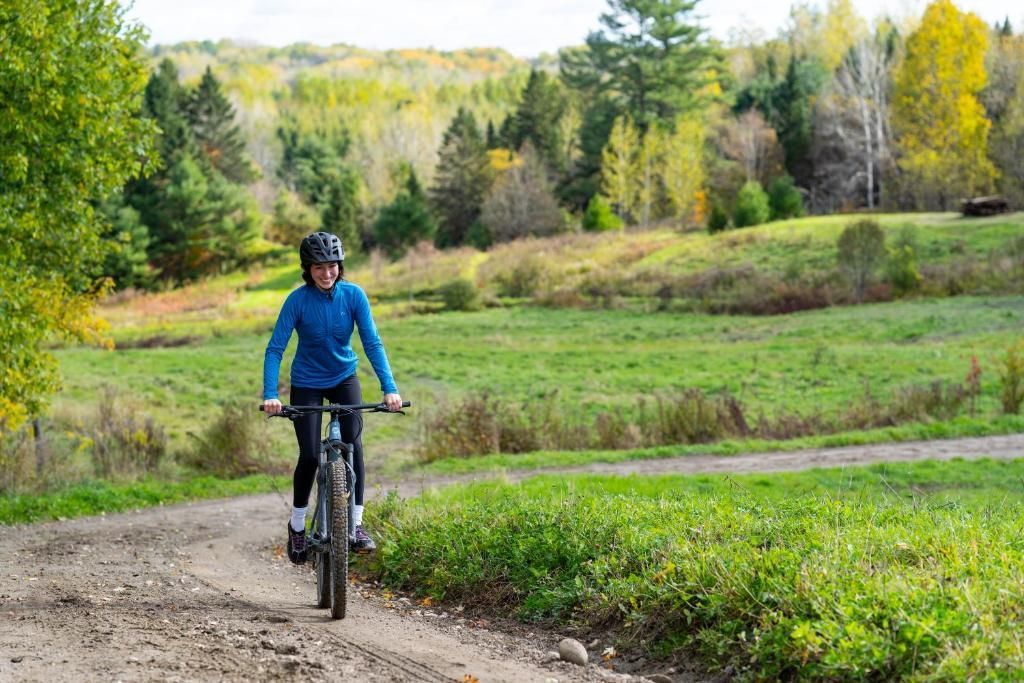 Een fietser in een blauwe jas rijdt over een onverhard pad door een groen, bosrijk landschap.