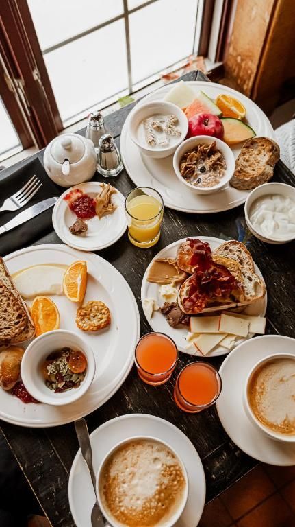 Ontbijt met pannenkoeken, gebak, fruit, koffie, sinaasappelsap en yoghurt op een tafel bij het raam.