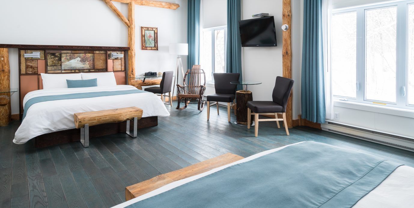 Lichte, moderne hotelkamer met een bed, zithoek, grote ramen en een blauw tapijt.