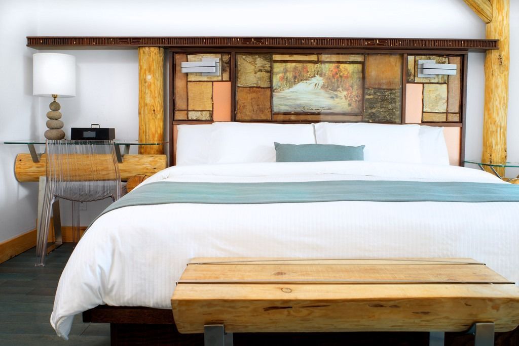 Lichte slaapkamer met een wit bed, een turquoise loper, rustieke houten accenten en een landschapsschilderij boven het hoofdeinde.