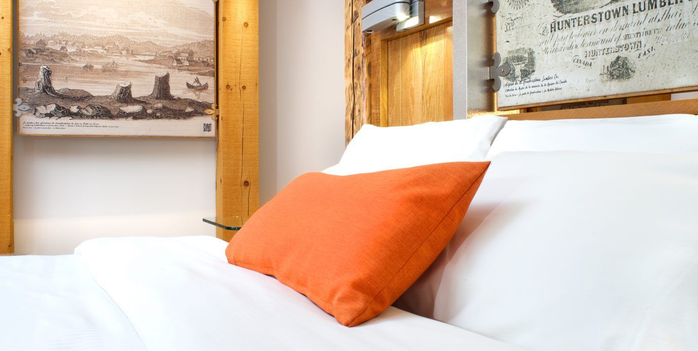 Wit bed met feloranje kussen in een gezellige kamer met ingelijste kunstwerken aan de muur.
