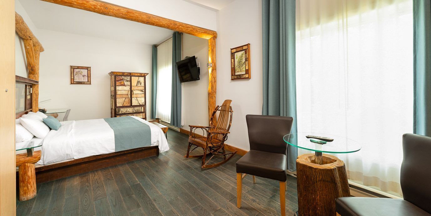 Gezellige slaapkamer met een bed, schommelstoel, bureau, tv en een groot raam met vitrage.