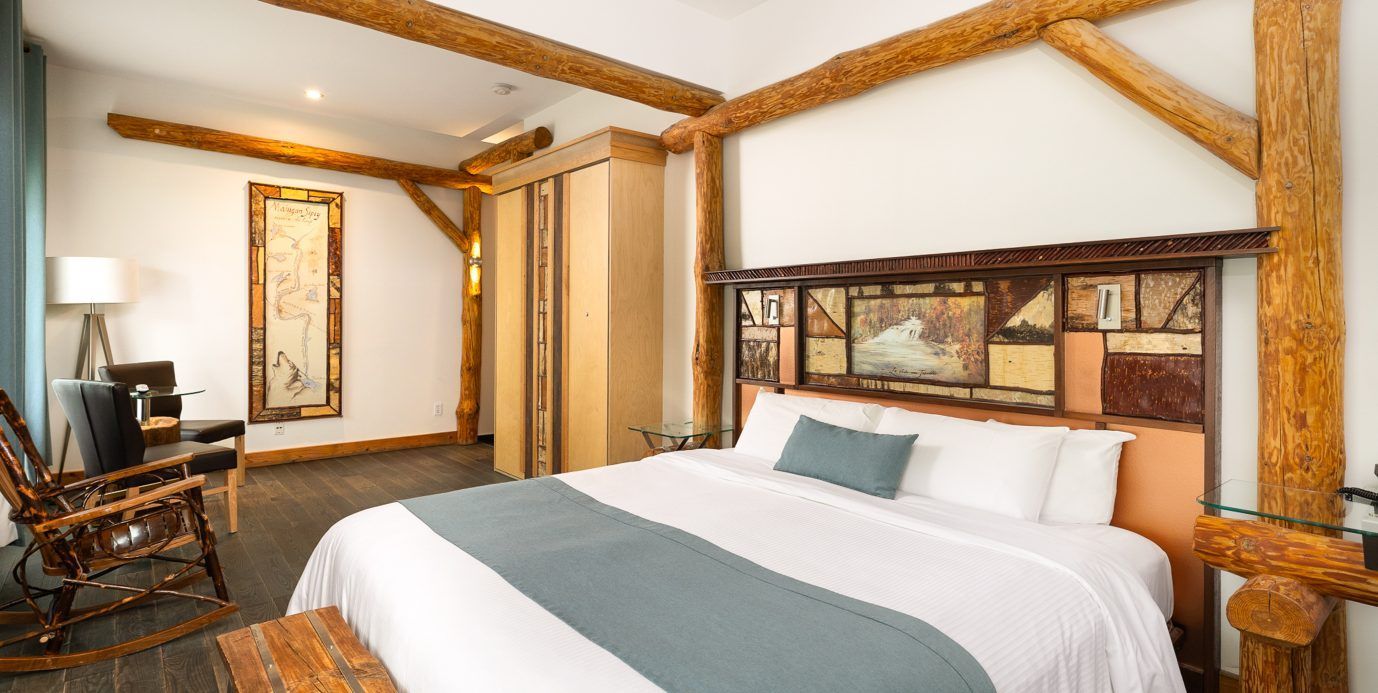 Ruime slaapkamer met een groot bed, houten balken en een spiegel bij het raam.