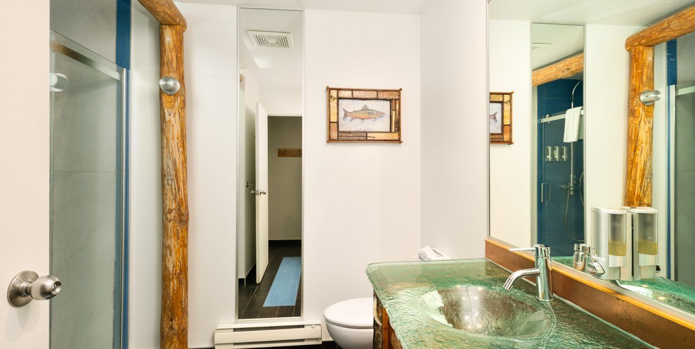 Lichte badkamer met goudkleurige spiegel, groene glazen wastafel, toilet en witte muren.