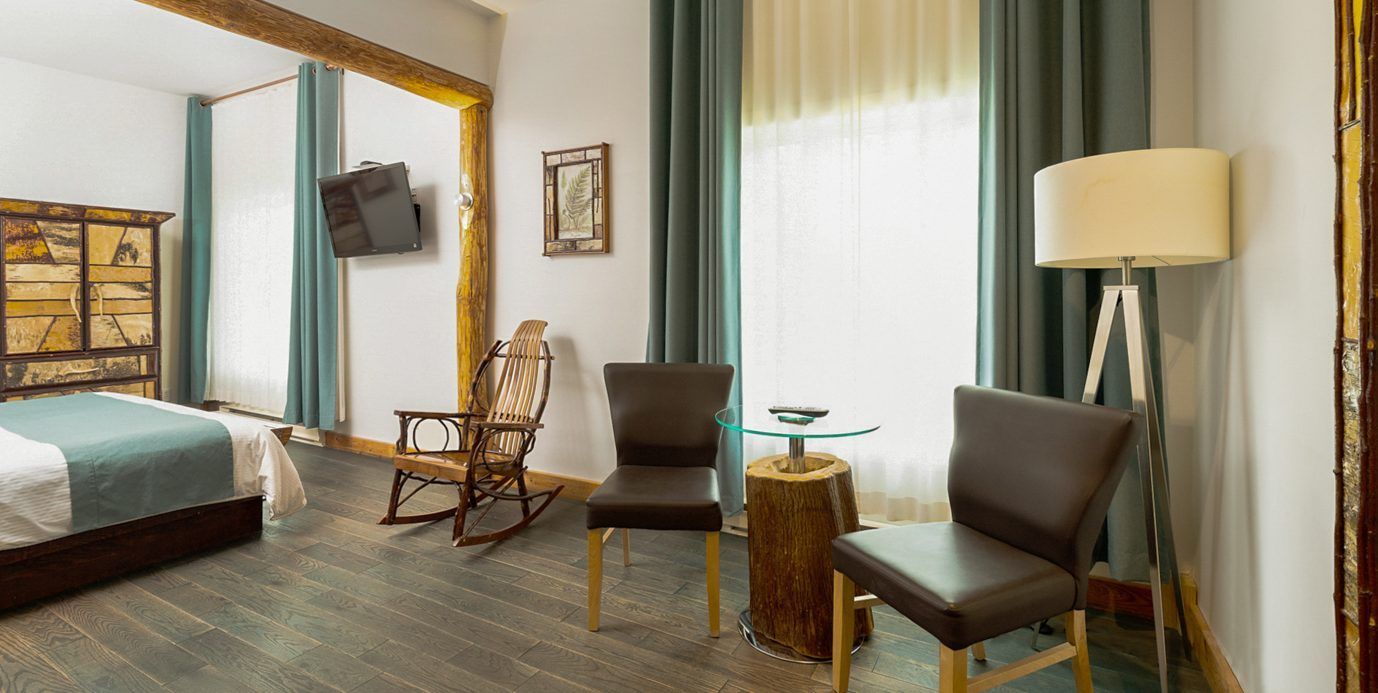 Moderne slaapkamer met een turquoise bed, een rieten stoel en twee fauteuils bij het raam.