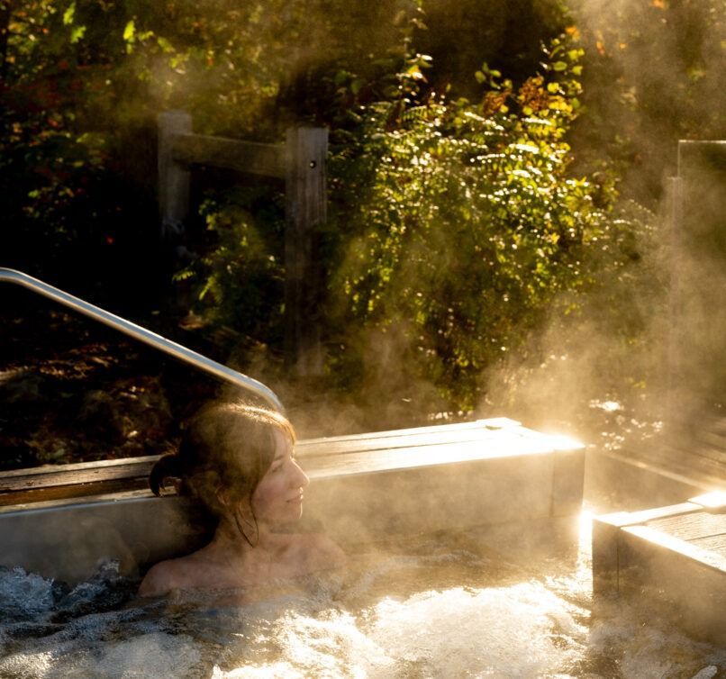 Iemand ontspant in een stomende buitenjacuzzi, omgeven door zonovergoten groen.