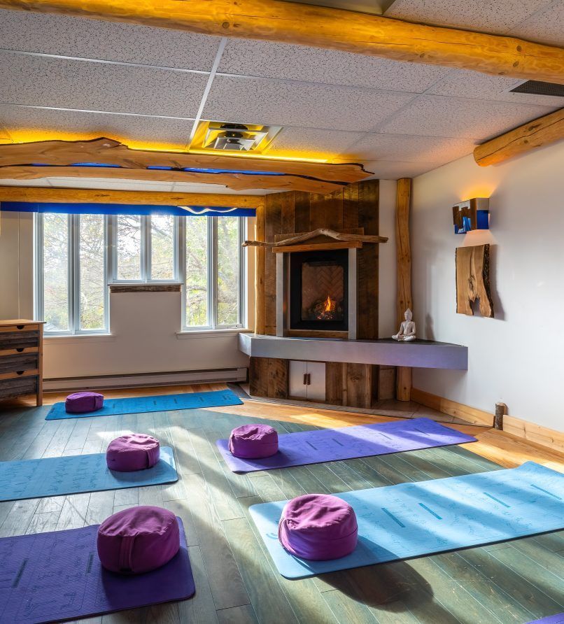 Een zonnige yogastudio met matten en paarse kussens op een houten vloer.