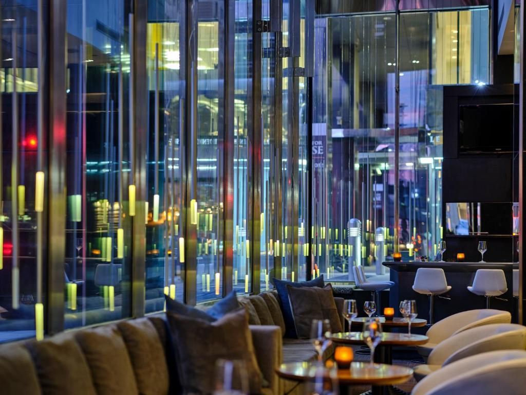 Moderne lounge met glazen wanden, uitzicht op de stadslichten en tafels gedekt met drankjes en kaarsen.