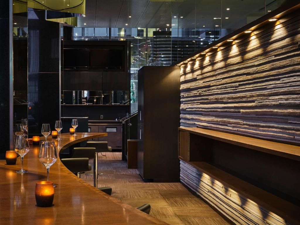 Moderne loungebar met houten toonbank, glazen verlicht door kaarsen en blauw verlichte, gestructureerde wandpanelen.