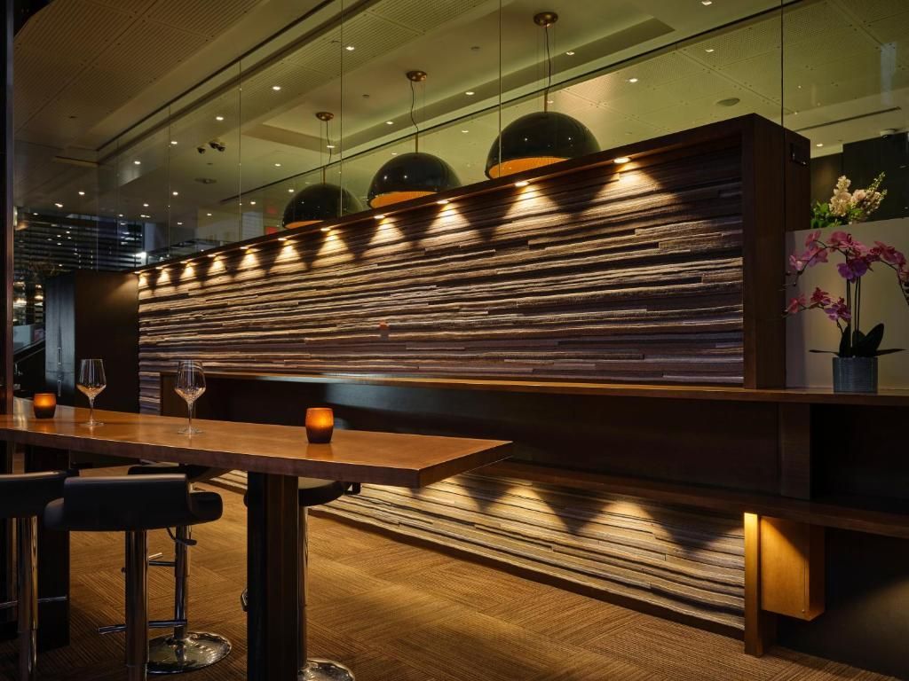 Modern restaurantinterieur met houten tafels, warme verlichting en een wand met textuur en achtergrondverlichting.