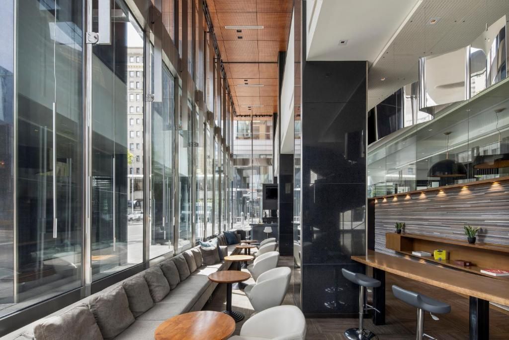 Modern café met ramen van vloer tot plafond, een houten plafond en barkrukken langs een lange glazen wand.