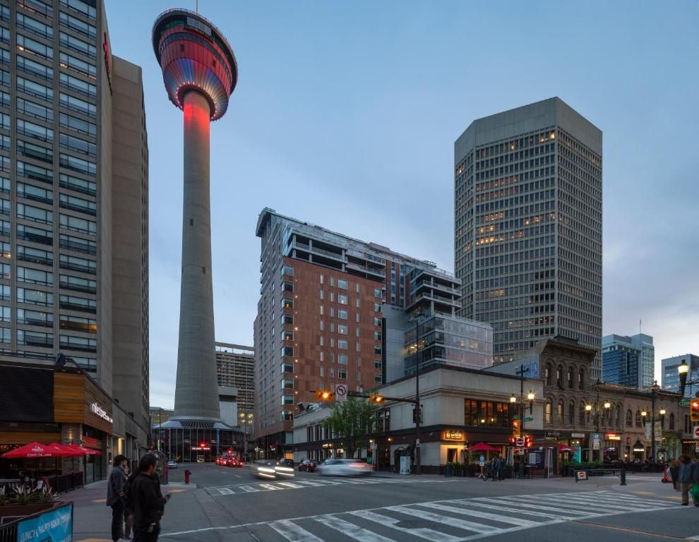 De CN Tower in Toronto bij schemering, met de stadsgebouwen bovenaan rood verlicht en een straatkruising eronder.