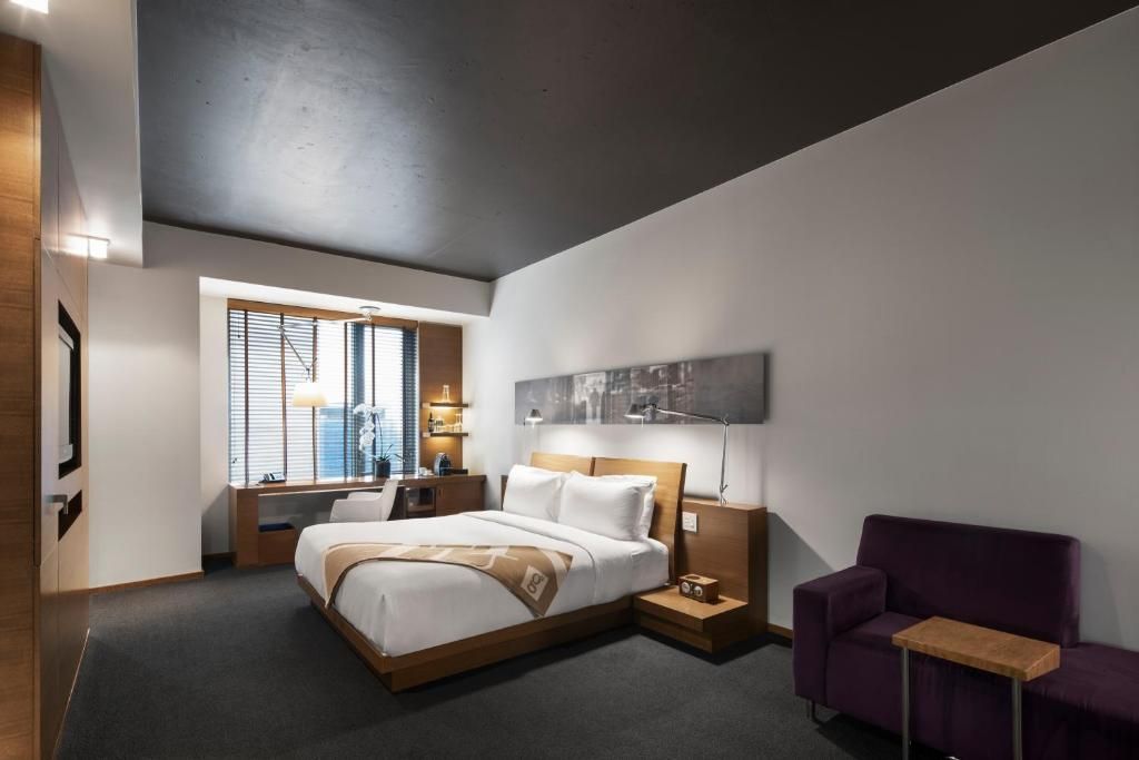 Moderne hotelkamer met een groot bed, paarse stoelen en een raam met uitzicht op de stad.