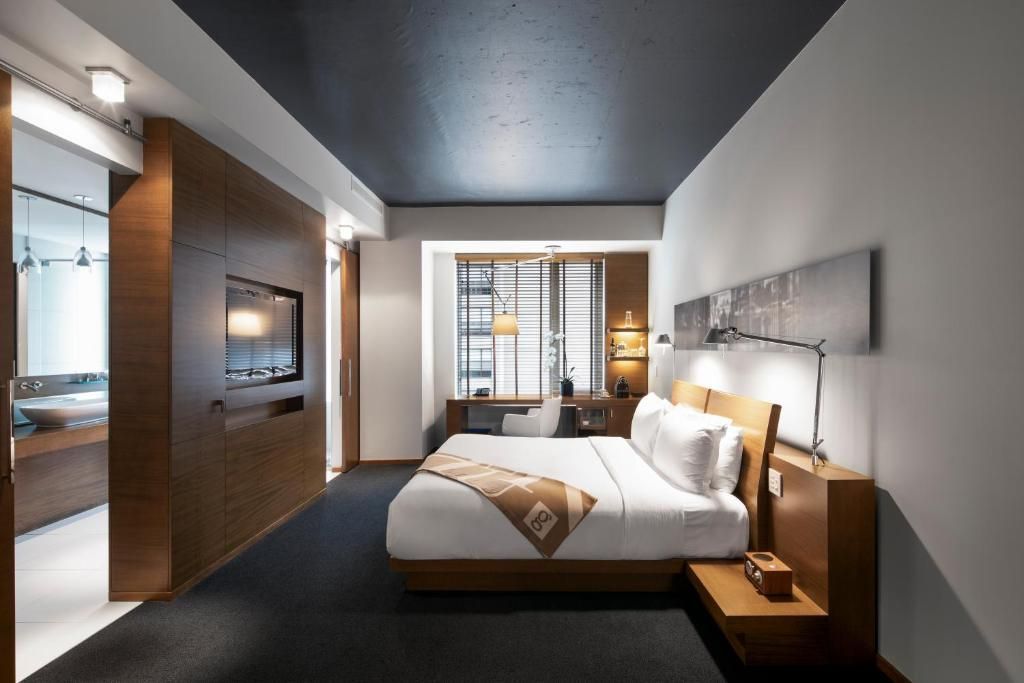 Moderne hotelkamer met een groot bed, donker plafond en warme houten accenten.