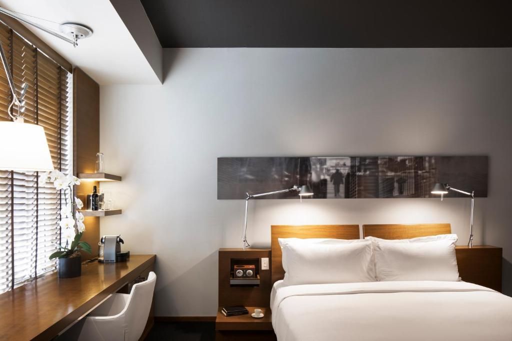 Moderne hotelkamer met queensize bed, houten bureau bij het raam en sfeervolle nachtverlichting.