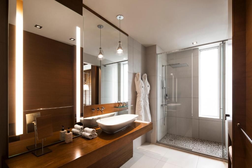 Moderne badkamer met houten badmeubel, opbouwspoelbak, spiegel en glazen douchecabine.