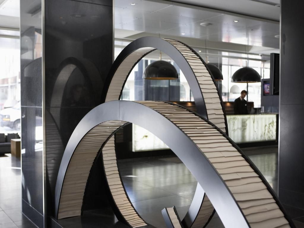 Abstracte houten boogsculptuur in een moderne binnenlobby met spiegelwanden en reflecties.