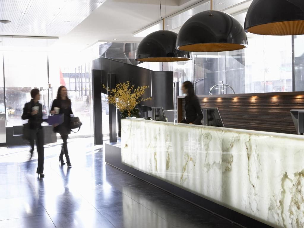 Moderne lobby met een marmeren receptiebalie, hanglampen en mensen die door een licht gebouw lopen.