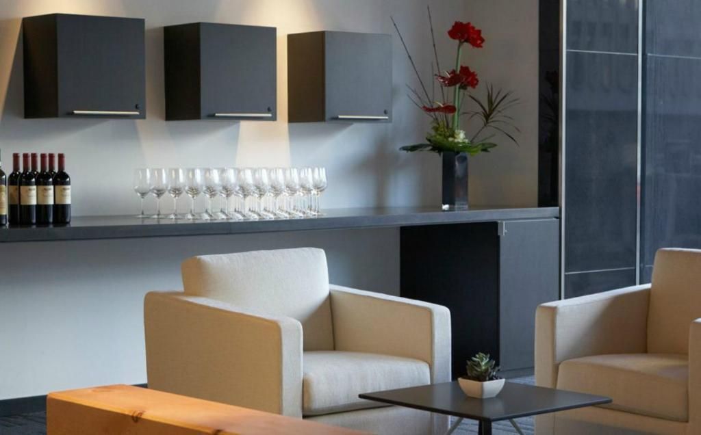 Moderne lounge met beige fauteuils, donkere kasten, wijnglazen en een rood bloemstuk.