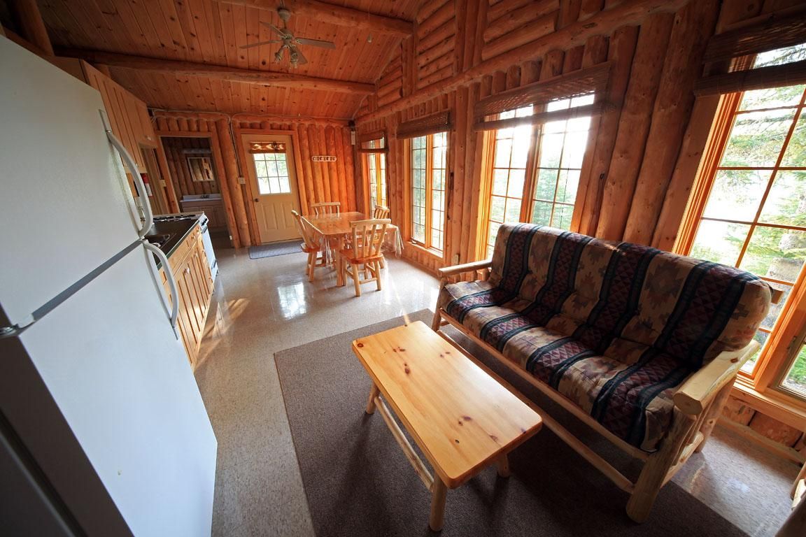 Houten woonkamer in een blokhut met bank, salontafel, stoelen en grote ramen met uitzicht op de bomen.