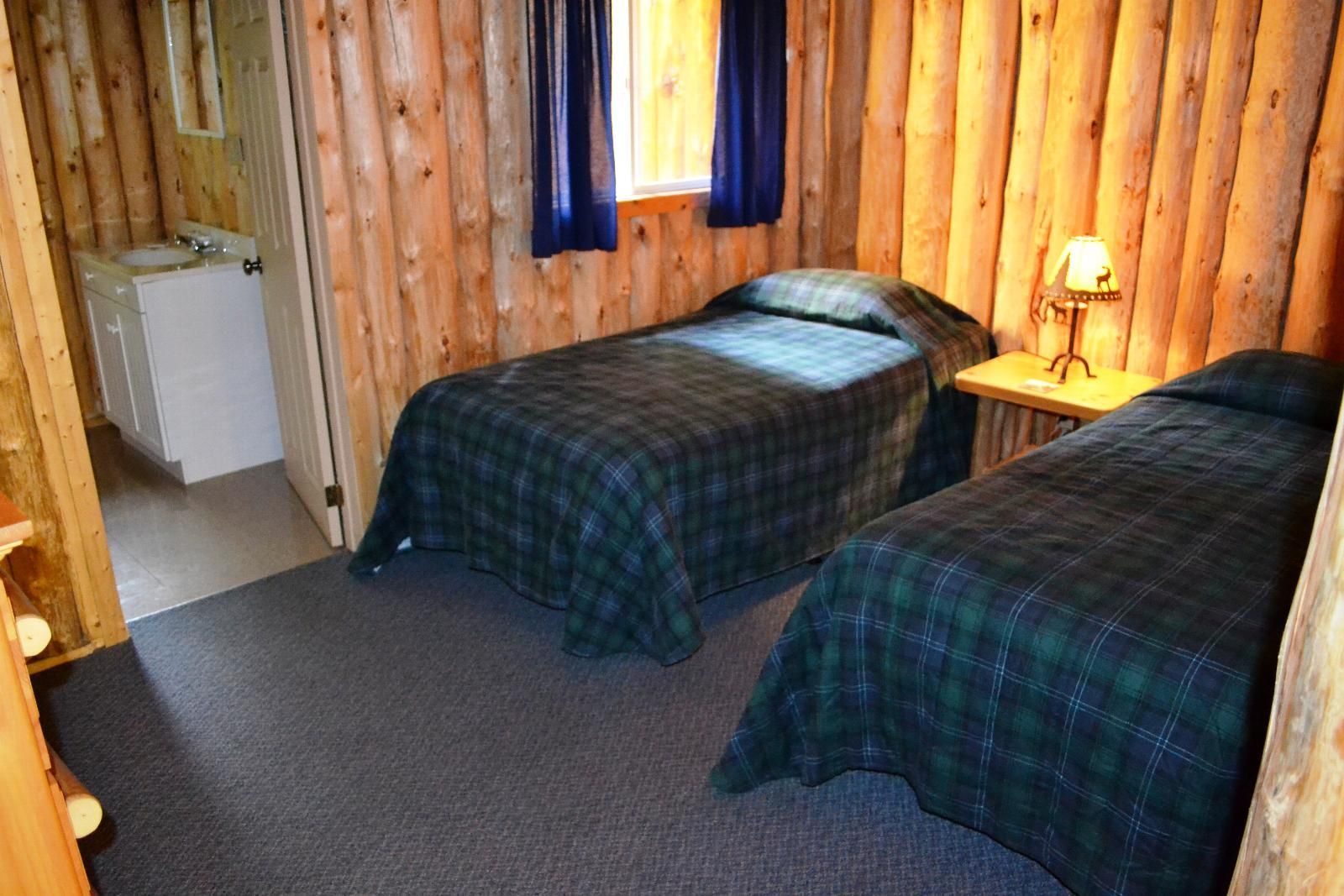 Kleine, rustieke slaapkamer met twee eenpersoonsbedden, houten lambrisering, blauwe gordijnen en een nachtlampje.