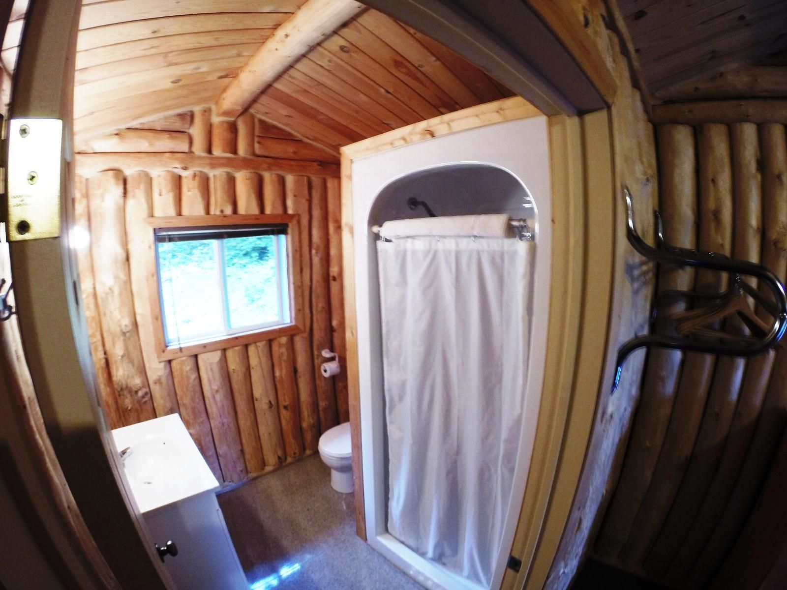 Rustieke houten badkamer met een douchegordijn en een klein raam dat uitzicht biedt op het interieur van de hut.