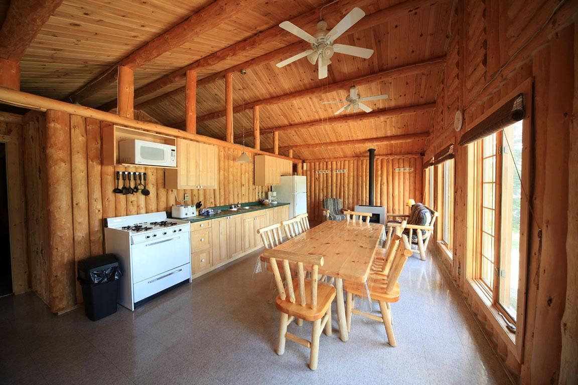 Rustieke houten keuken en eethoek met lange tafel, stoelen, fornuis en grote ramen.