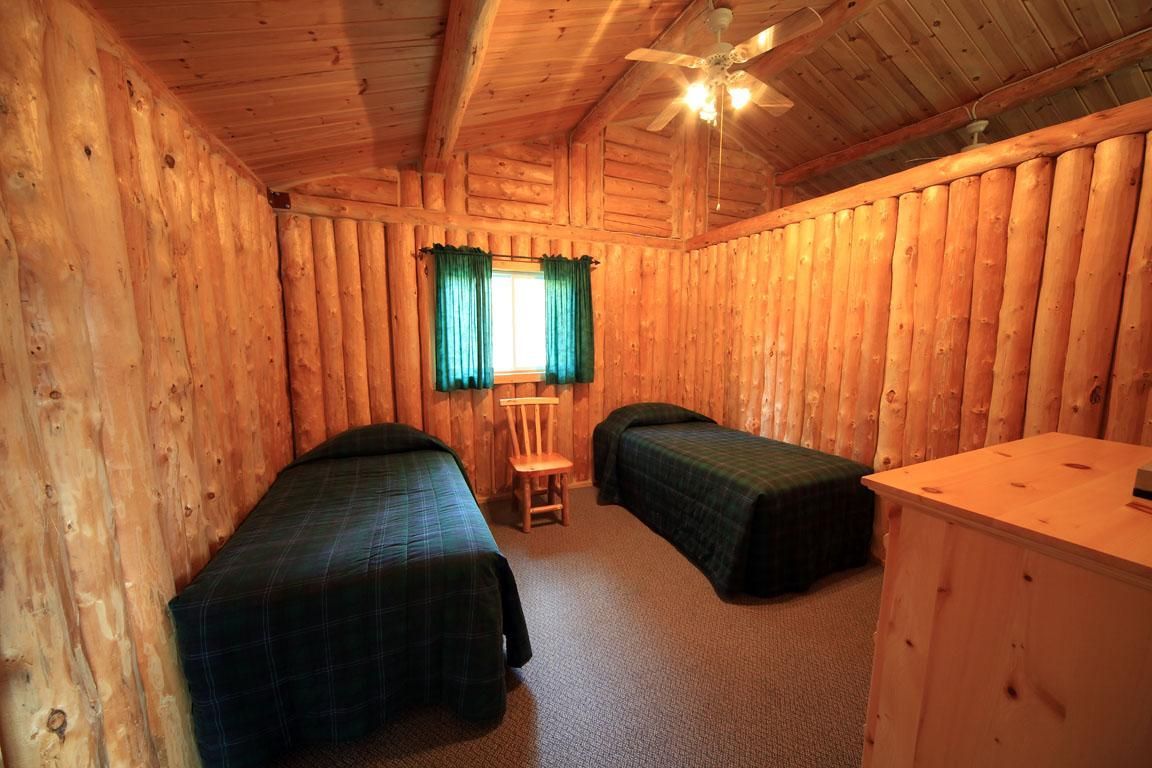 Houten slaapkamer in een blokhut met twee eenpersoonsbedden, een klein raam en een houten dressoir.