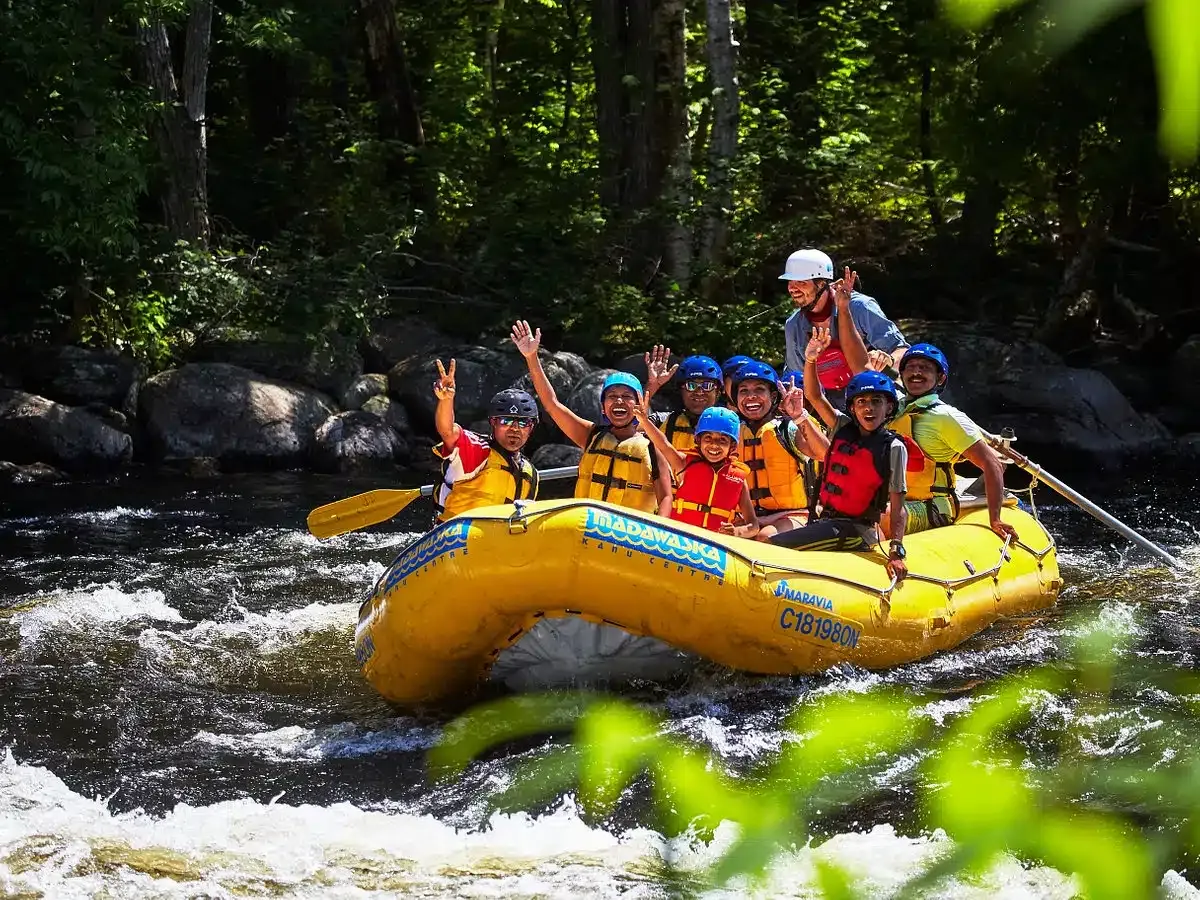 Een groep rafters in een gele raft ploetert door de stroomversnellingen van een rivier in een bosrijk gebied.