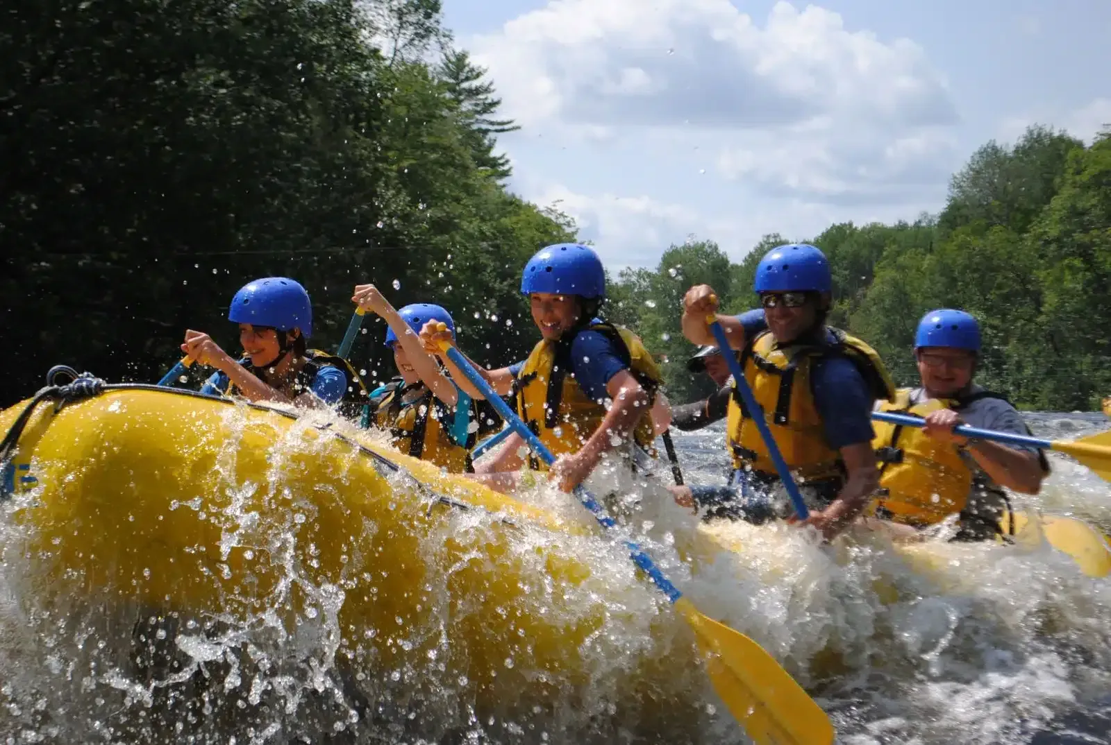 Een raftingteam met blauwe helmen ploetert in een gele raft door wildwaterstroomversnellingen.