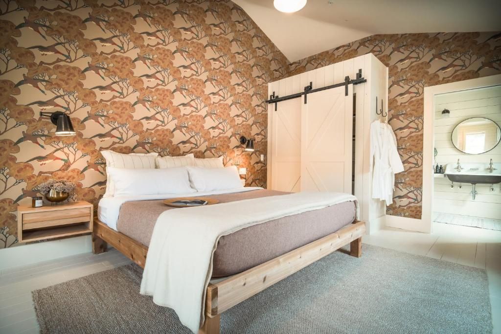 Gezellige slaapkamer met een wit bed, behang met een patroon, een nachtkastje en een ronde spiegel boven een kaptafel.