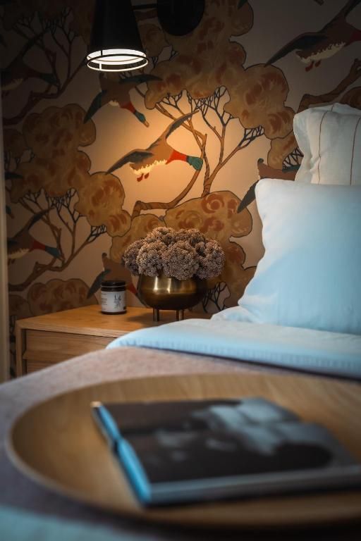 Gezellige slaapkamer met behang met patroon, nachtlampje, bloemen en een bed met blauw beddengoed.