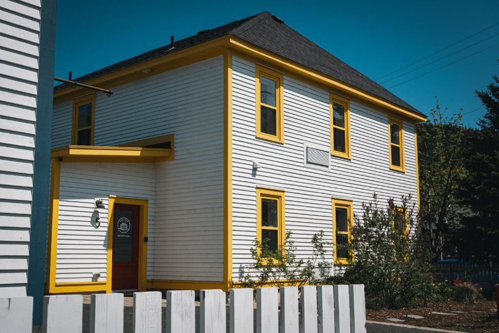 Wit, twee verdiepingen tellend huis met gele kozijnen en luiken, gezien vanaf de voorkant onder een helderblauwe hemel.