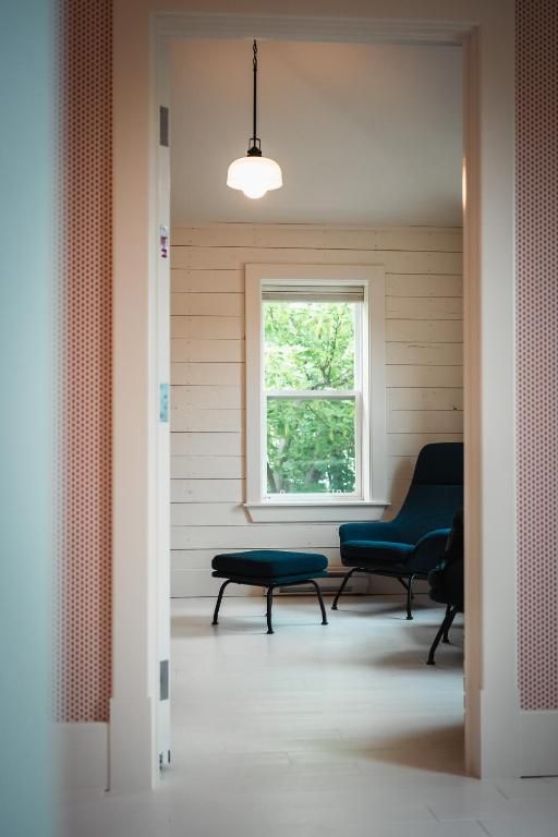 Een lichte kamer met een hanglamp, een raam en een donkere fauteuil met voetenbank.