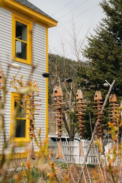 Huis met gele kozijnen, een wit houten hek en rustieke tuinsculpturen ervoor.