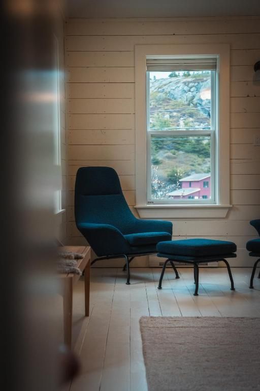 Minimalistische kamer met een turquoise stoel en voetenbank bij een raam met uitzicht op een stadje op een heuvel.