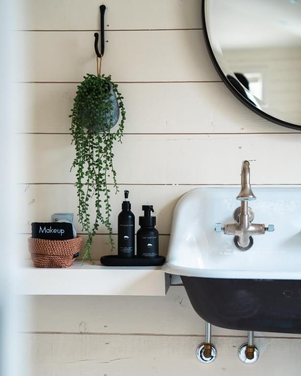 Badkamermeubel met witte wastafel, zwart plankje, hangplant en toiletartikelen onder een ronde spiegel.