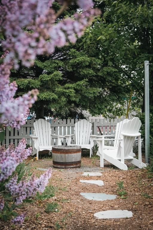 Gezellige zithoek in de tuin met witte stoelen, een houten tafel van een vat en een stenen pad onder bloeiende takken.