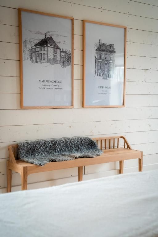 Minimalistische kamer met twee ingelijste schetsen boven een houten bankje met een grijze bontplaid.