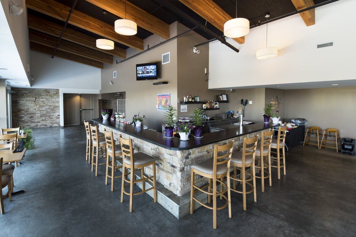 Modern café-interieur met een lange stenen bar, houten barkrukken, hanglampen en een aan de muur gemonteerde tv.