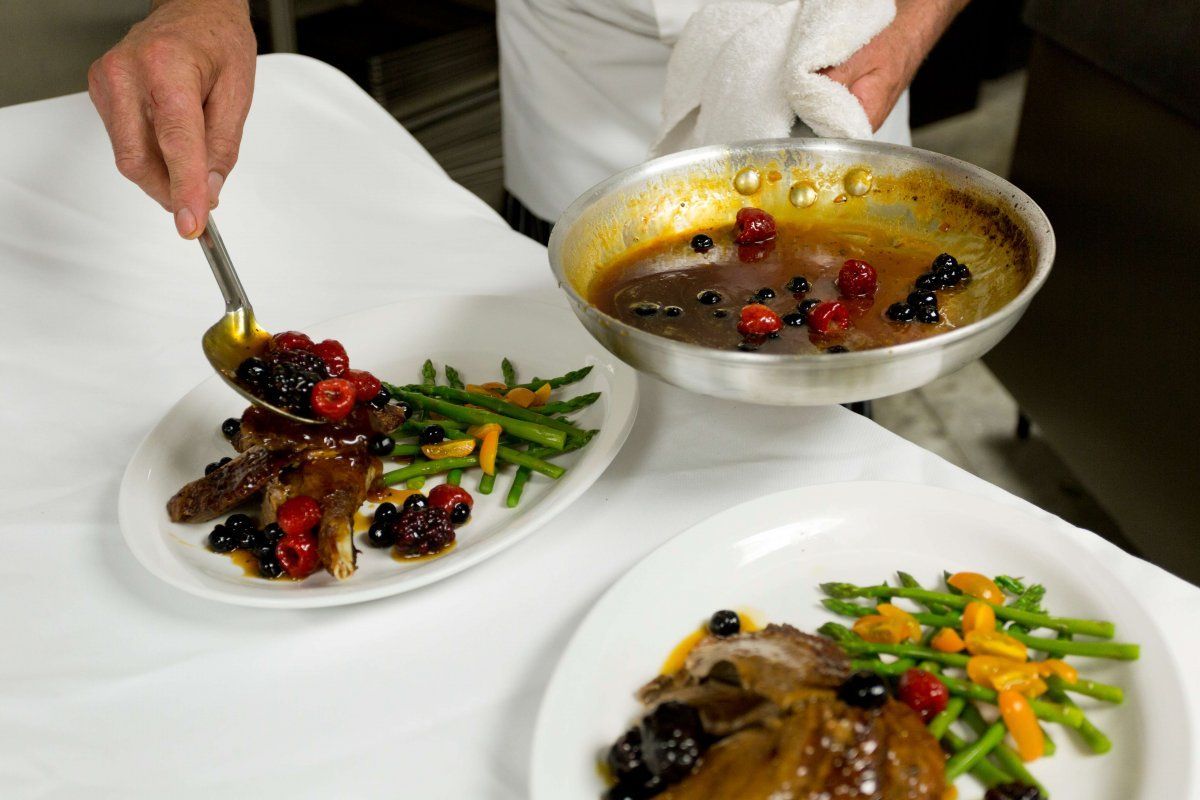 Een chef-kok schikt kleurrijke gastronomische gerechten op witte borden met bessensaus in een keuken.