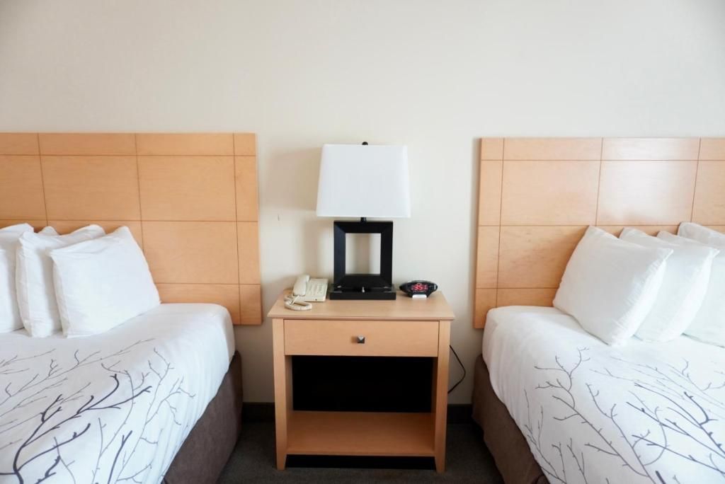 Twee keurig opgemaakte eenpersoonsbedden met wit beddengoed en een nachtkastje ertussen in een hotelkamer.