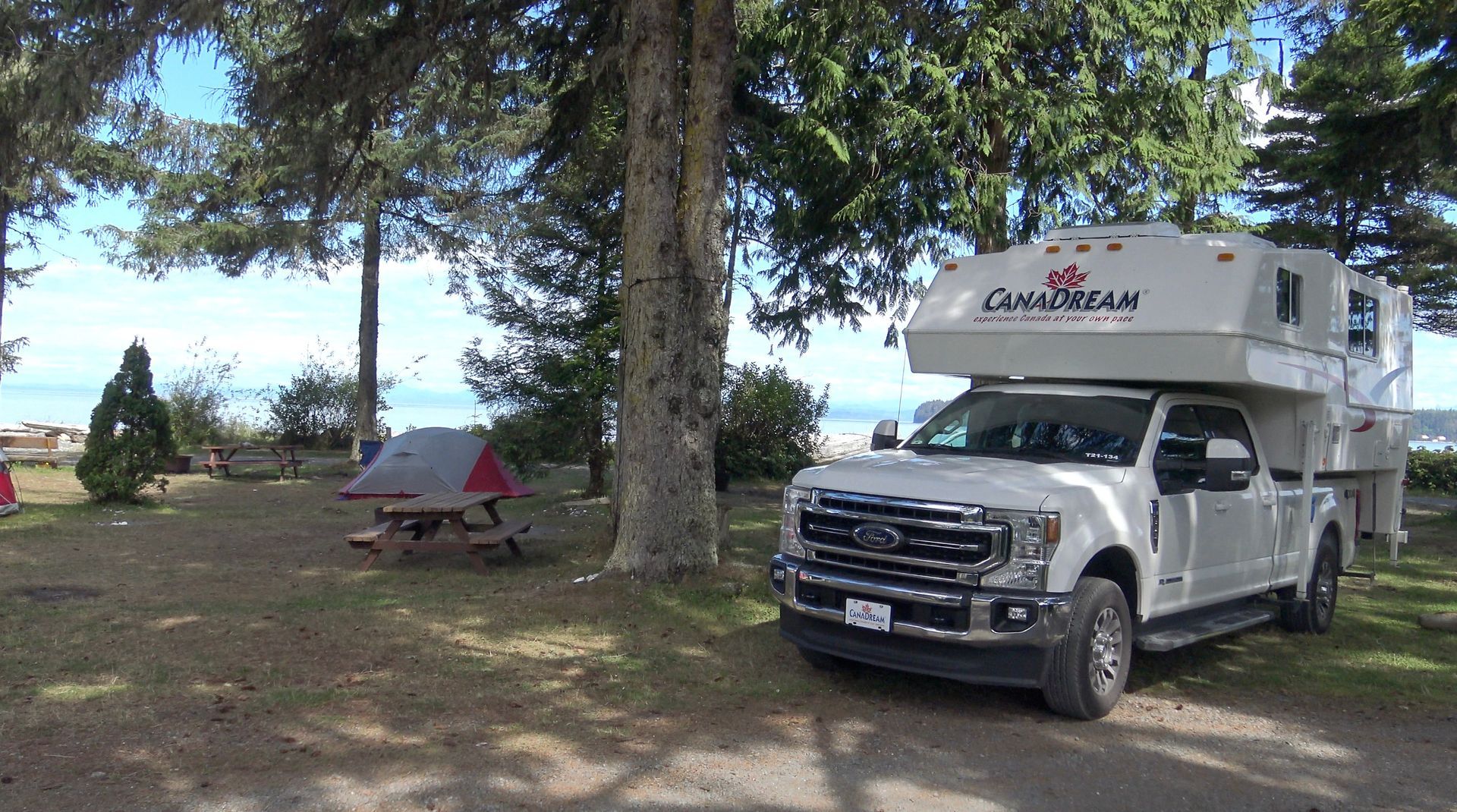 Maxi Travel 4x4 Camper geparkeerd bij bomen op een groene camping, met een picknicktafel