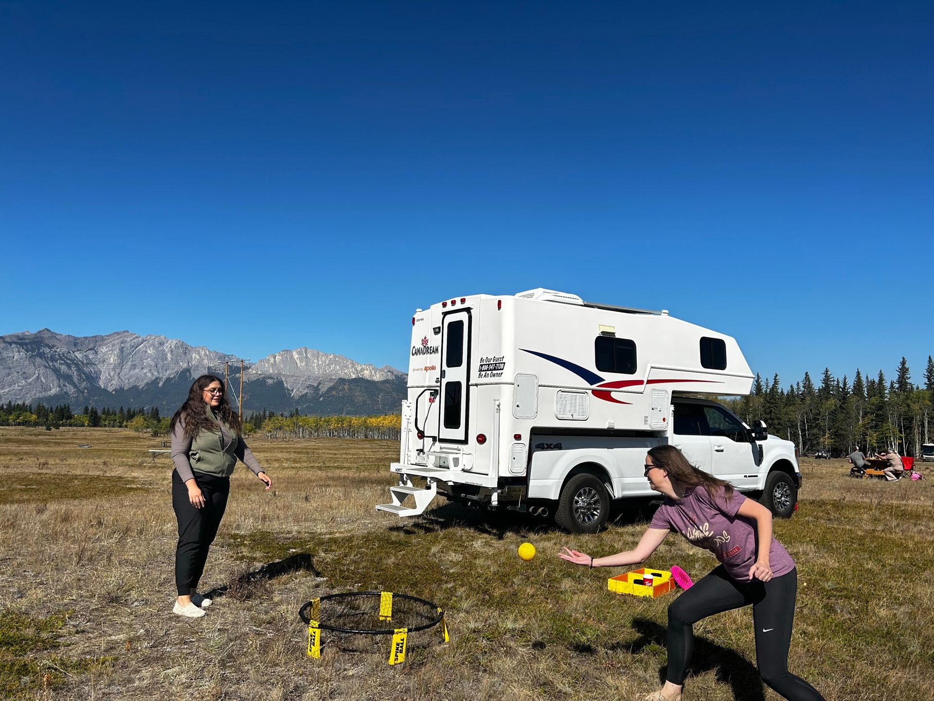Twee mensen spelen cornhole naast een Maxi Travel 4x4 Camper