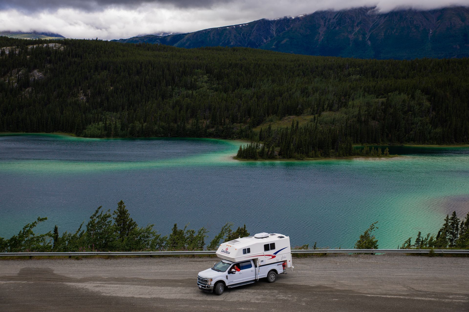 Maxi Travel 4x4 Camper geparkeerd bij een turquoise meer met beboste bergen op de achtergrond