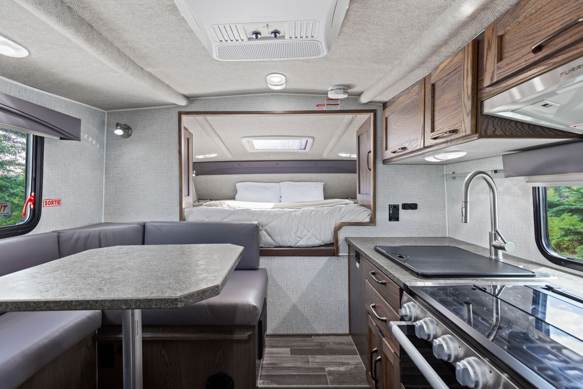 Compact camperinterieur van een Maxi Travel 4x4 Camper met grijze bank, keukenblad en slaapnis achterin