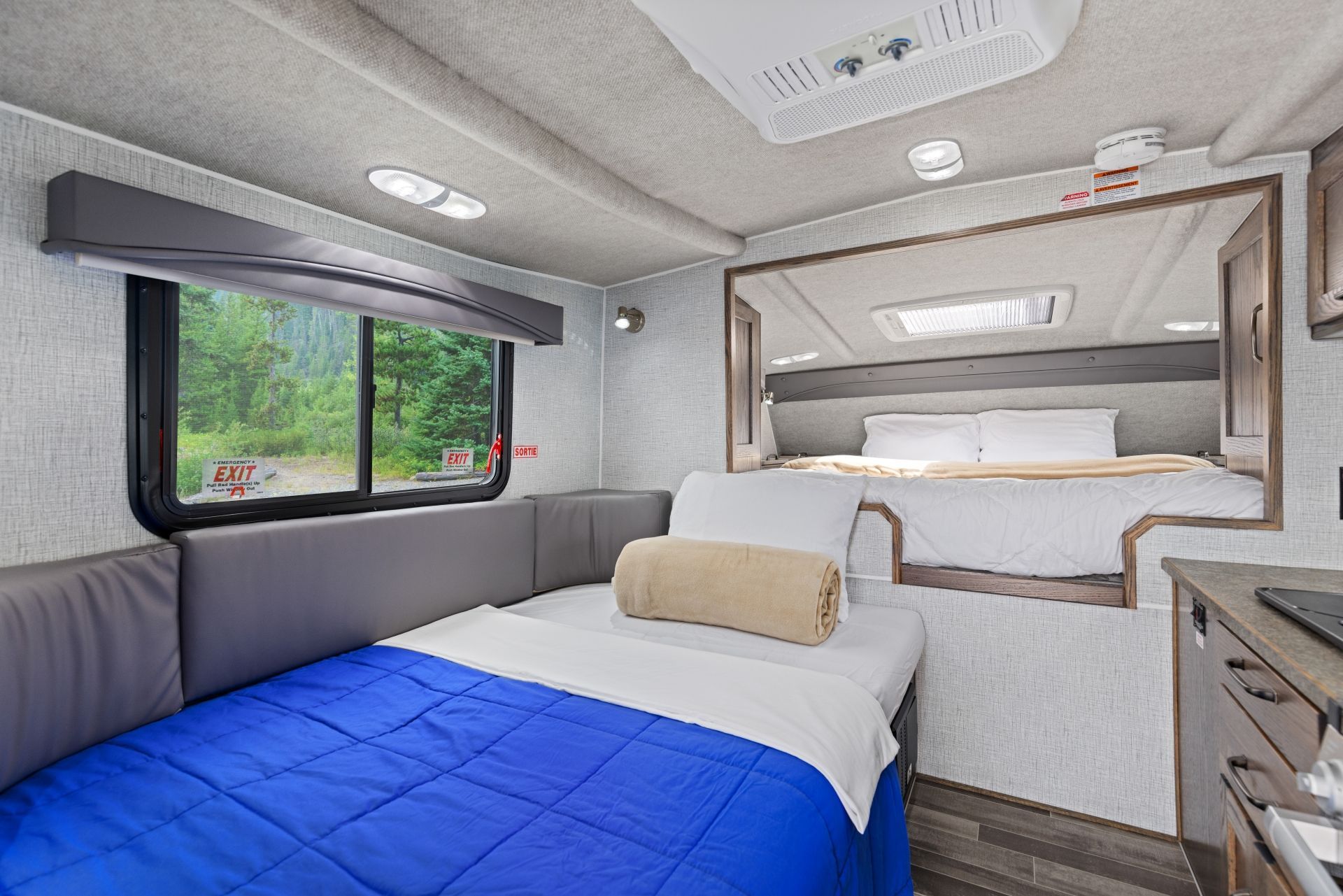 Compact interieur van een Maxi Travel 4x4 Camper met twee bedden, grijze meubels en een raam met groen uitzicht
