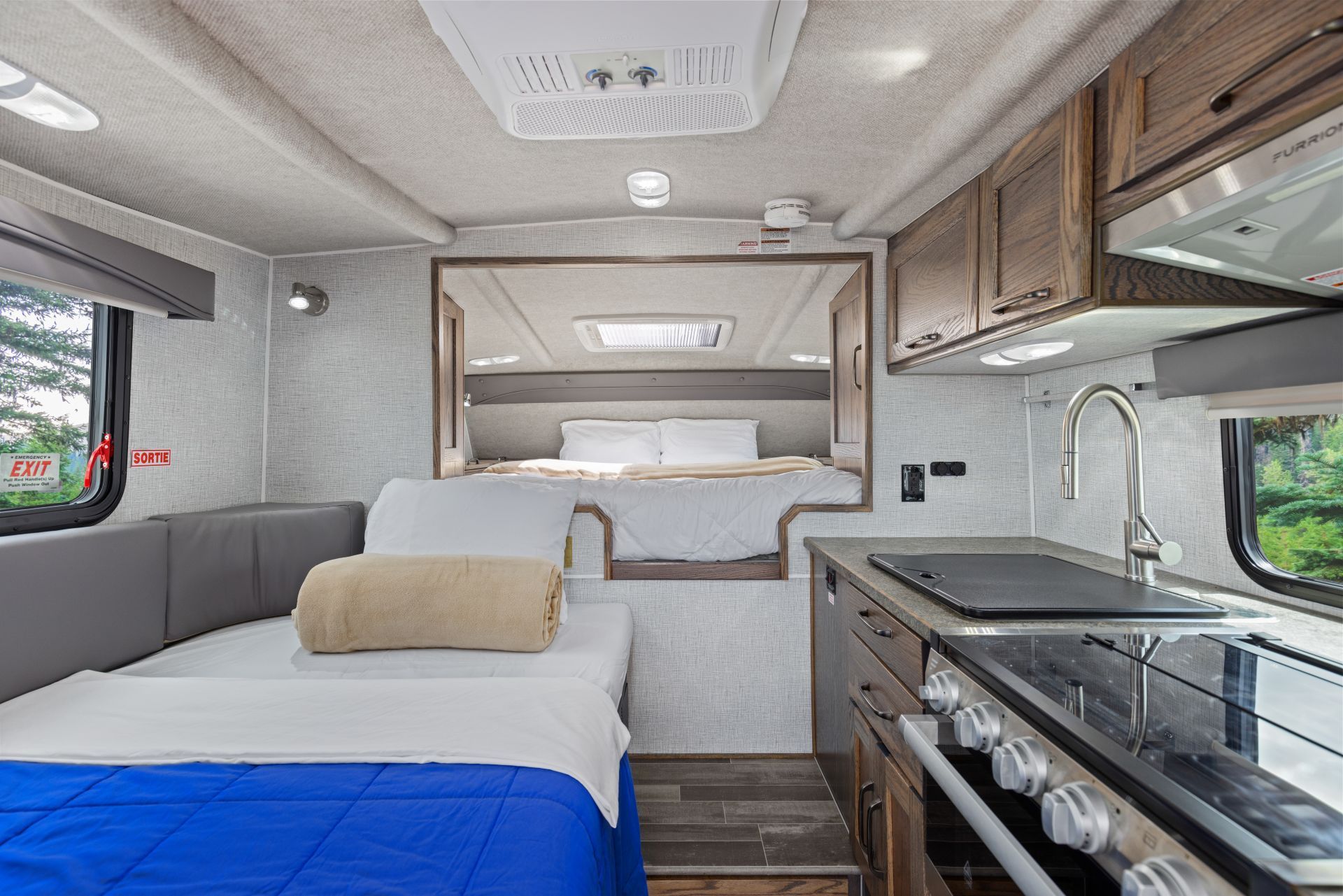 Compact interieur van een Maxi Travel 4x4 Camper met bed, kitchenette, bovenkastjes en een grijze zithoek