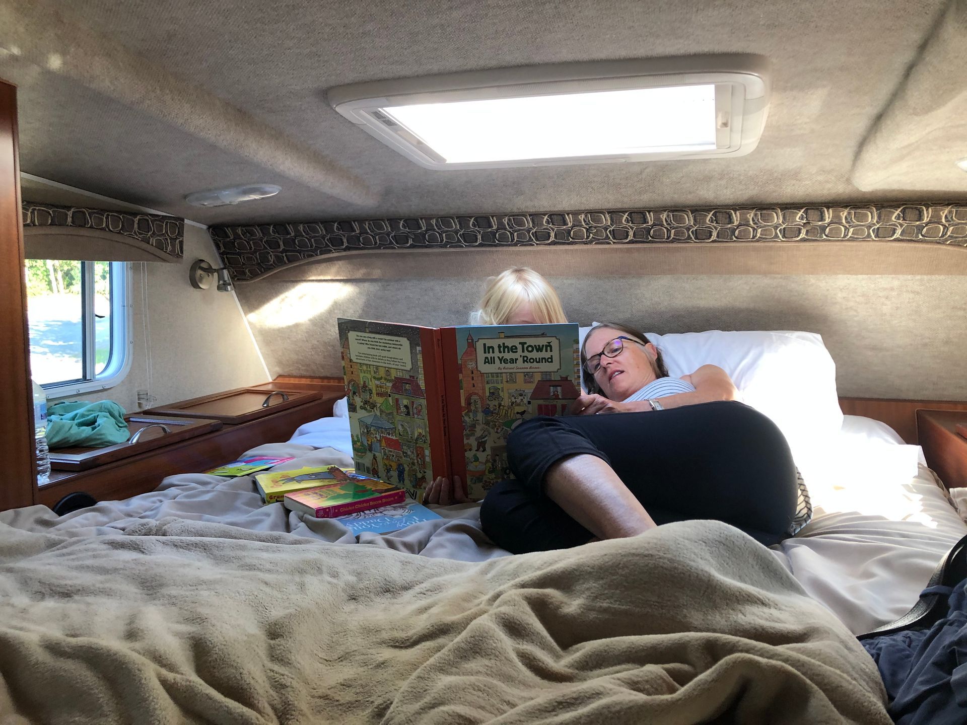 Persoon die leest in een knus slaaphoekje in een Maxi Travel 4x4 Camper, met boeken en zachte dekens.