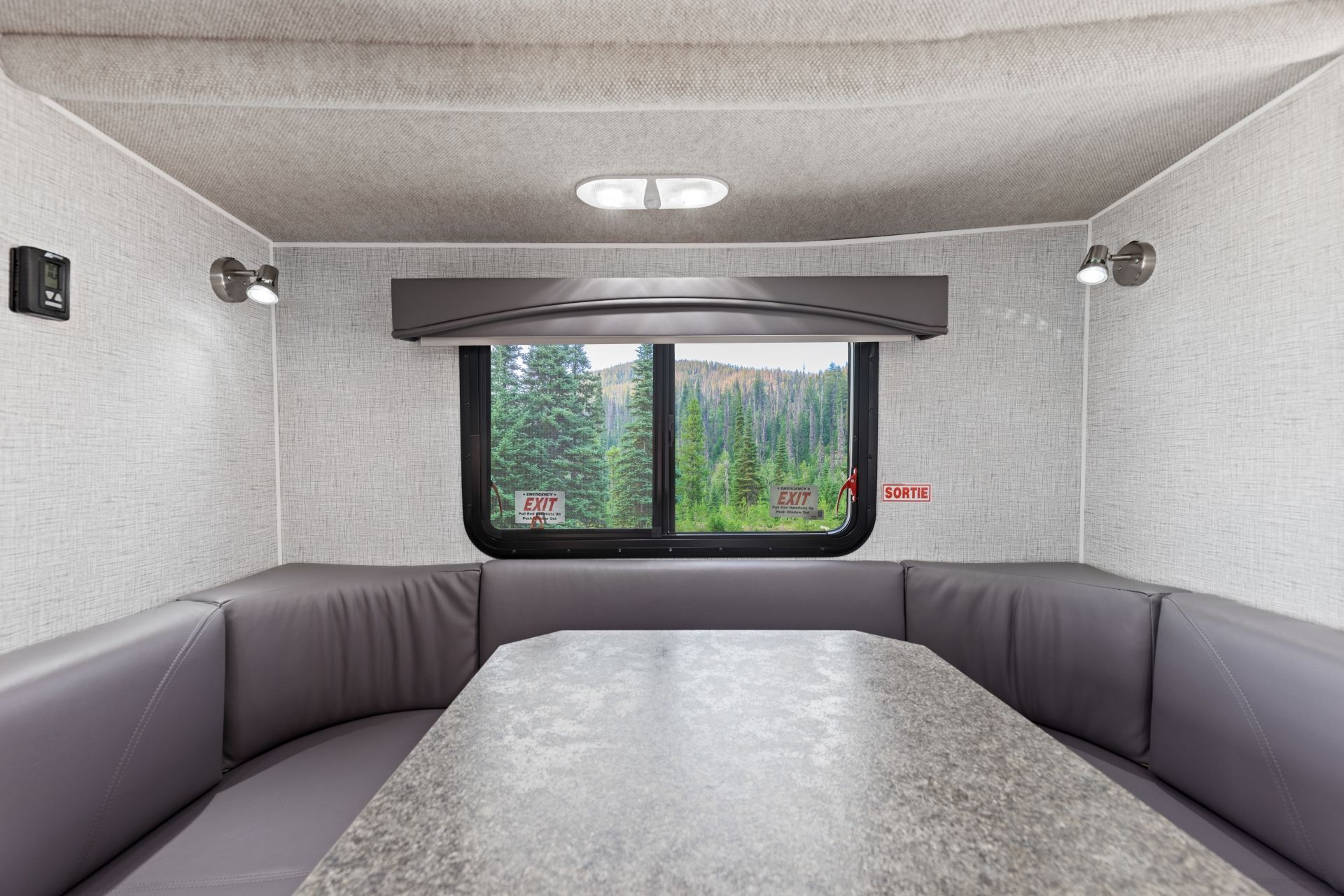 Grijs interieur van een Maxi Travel 4x4 Camper met een zitgroep en uitzicht door het raam op bomen en bergen
